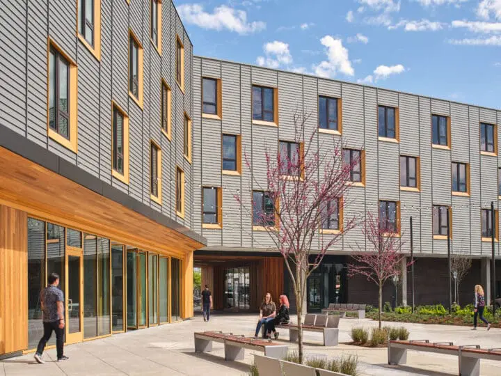 A man walks in front of 72Foster’s ground-floor community room’s Nana Walls while two women sit on a bench.