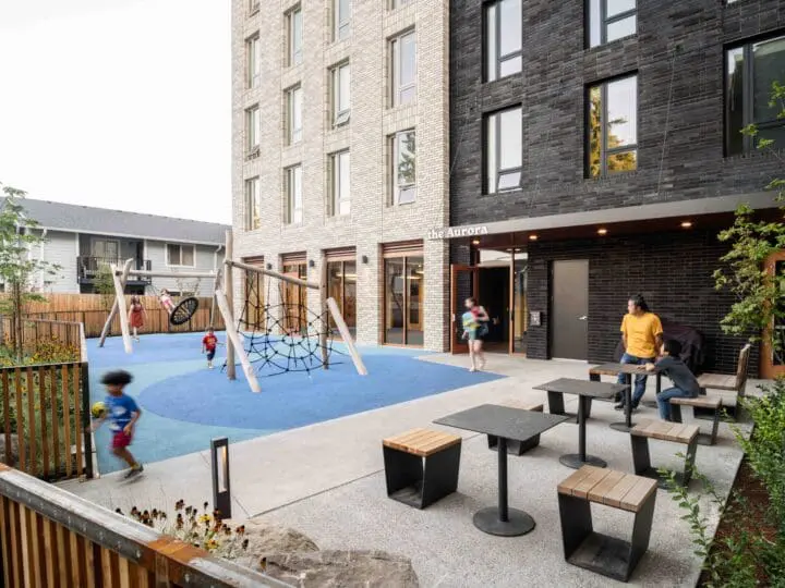 Kids are running around and playing in an outdoor, fenced-in play area at The Aurora.