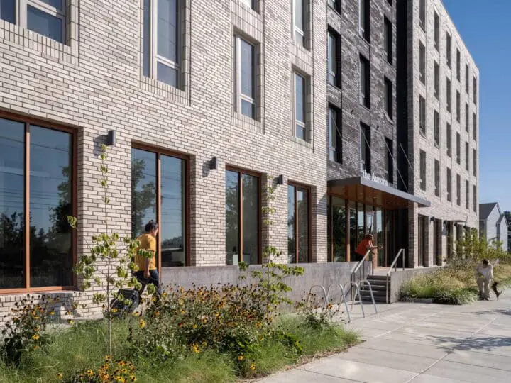 A person in a yellow shirt walks up the ramp to the front door of the apartment building, The Aurora.